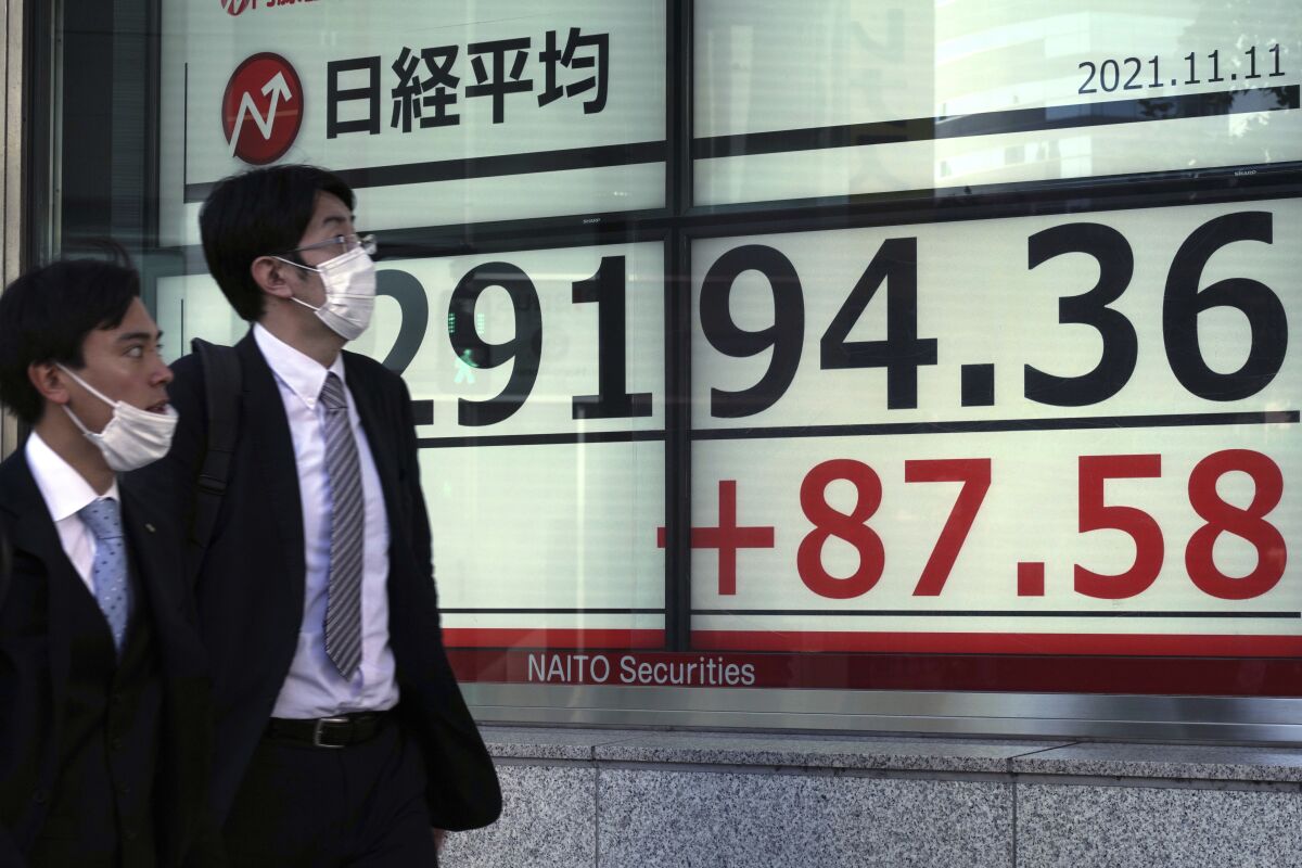 Men wearing protective masks walk in front of an electronic stock board showing Japan's Nikkei 225 index at a securities firm Thursday, Nov. 11, 2021, in Tokyo. (AP Photo/Eugene Hoshiko)