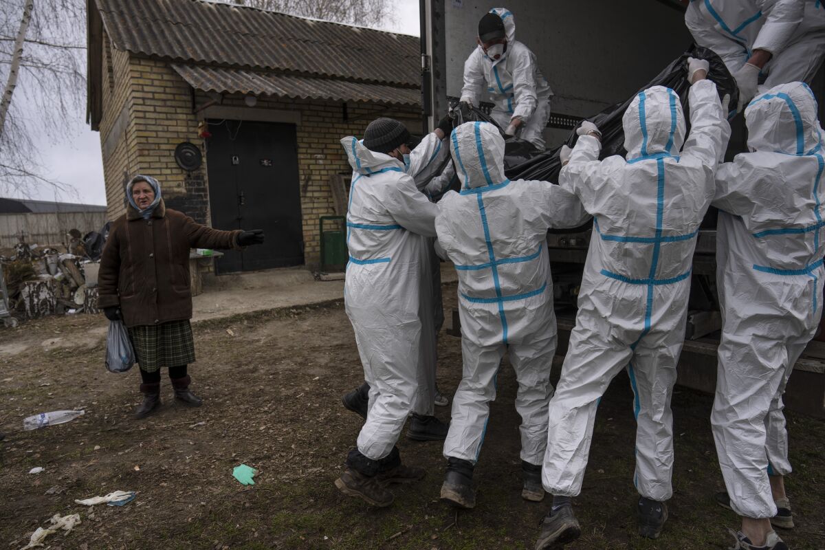 Nadiya Trubchaninova, 70, left, stands next to volunteers while loading a plastic bag that contains the body of a civilian killed by Russian soldiers into a truck, in Bucha, in the outskirts of Kyiv, Ukraine, Tuesday, April 12, 2022. (AP Photo/Rodrigo Abd)