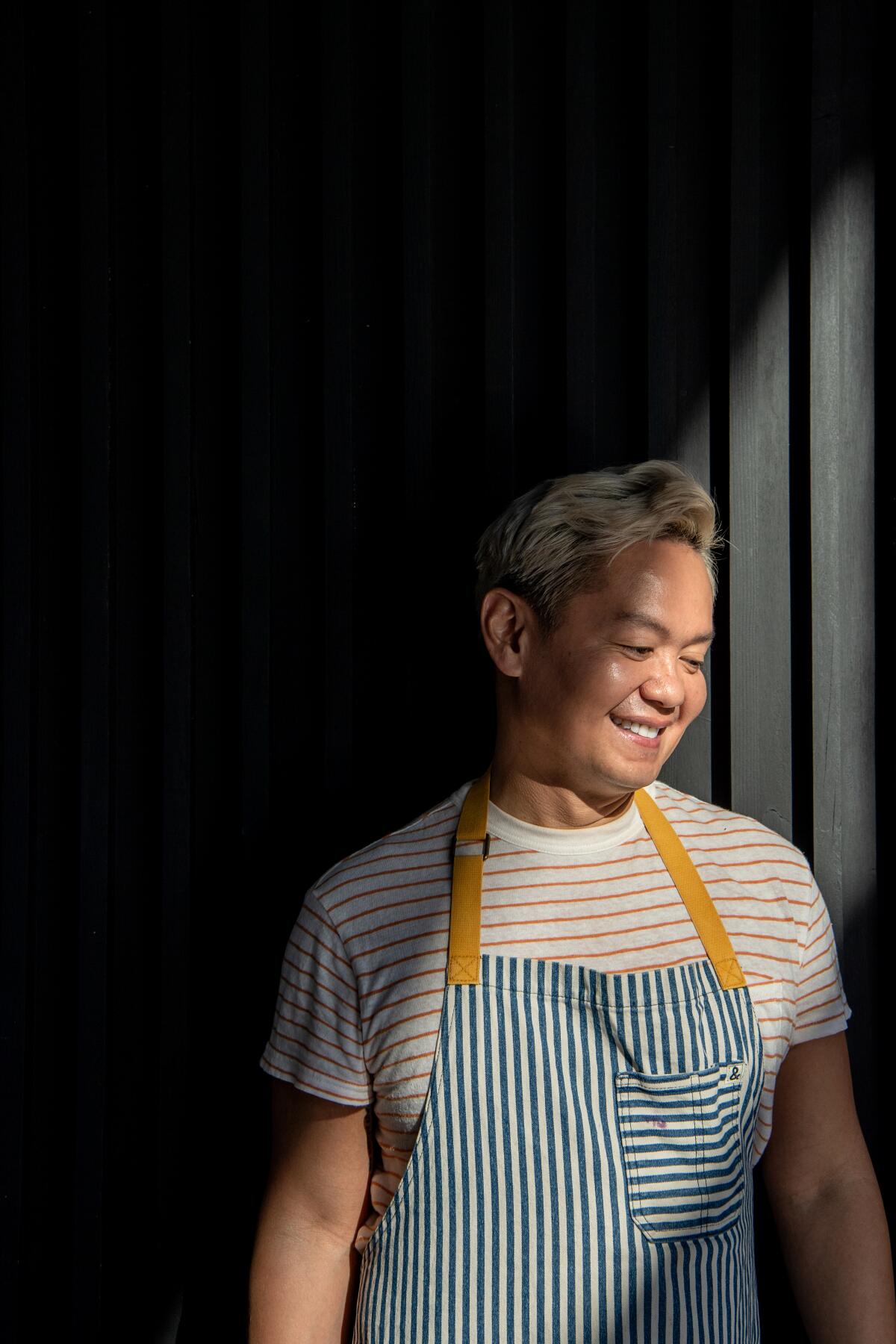 A smiling man in an apron with a deep angled shadow.