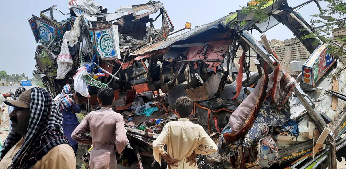 Local residents look at the wreckage of a bus at the site of an accident near Dera Ghazi Khan, Pakistan, Monday, July 19, 2021. A speeding bus carrying mostly laborers traveling home for a major Muslim holiday rammed into a container truck on a busy highway in central Pakistan, killing and injuring dozens, police and rescue officials said. (AP Photo/Saleem Khan)
