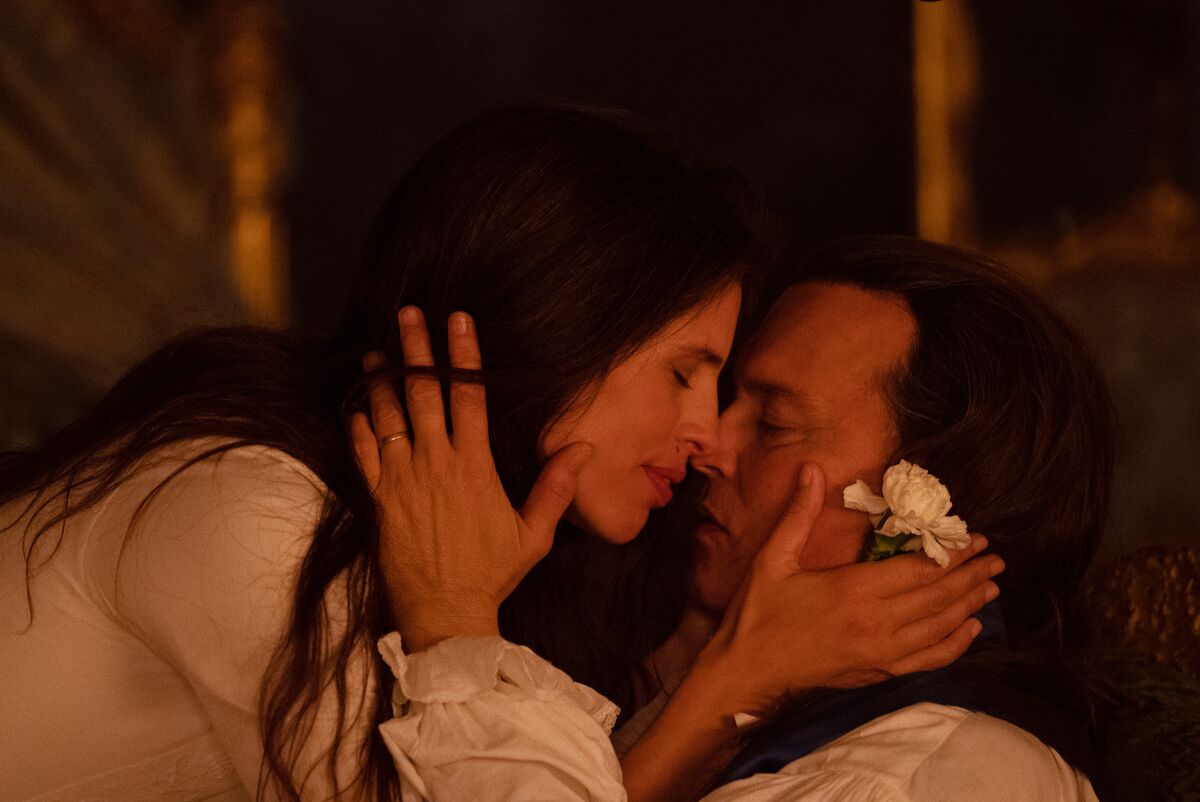 A man and a woman, nose to nose, eyes closed, with their hands on each other's faces.