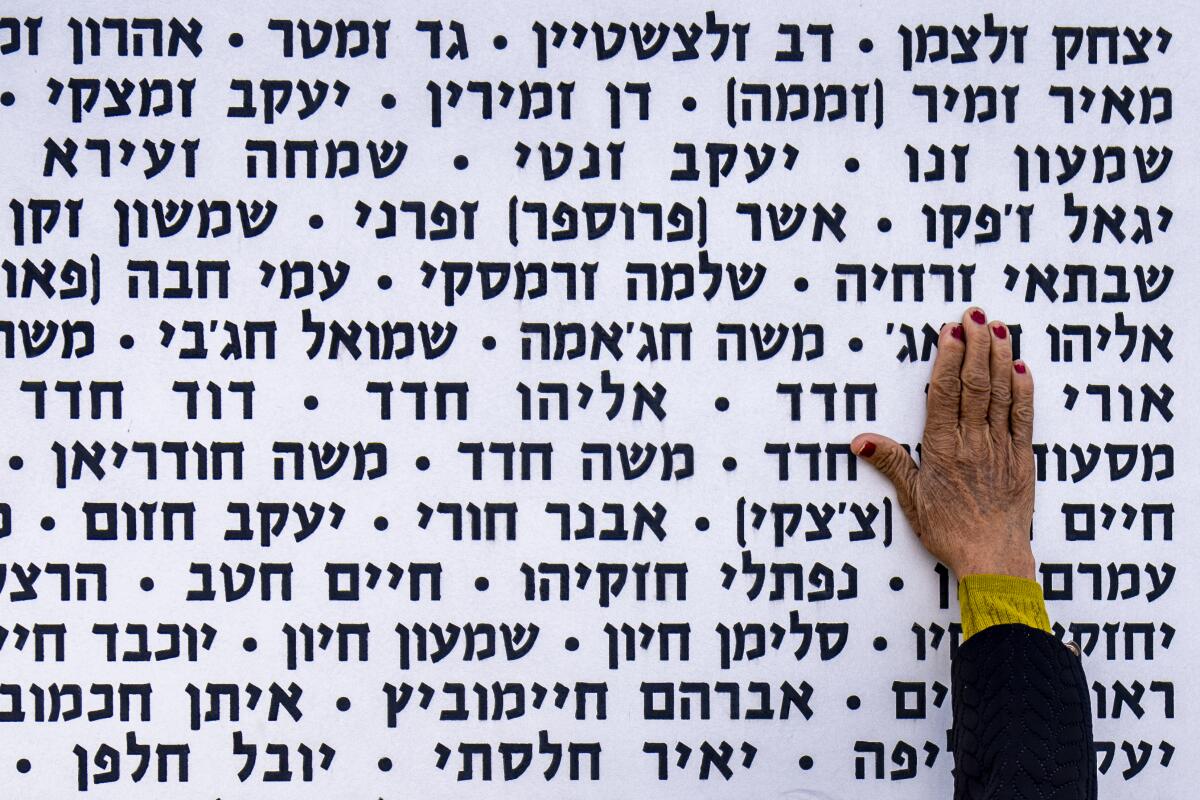 Una mujer toca la pared con los nombres de soldados israelíes fallecidos