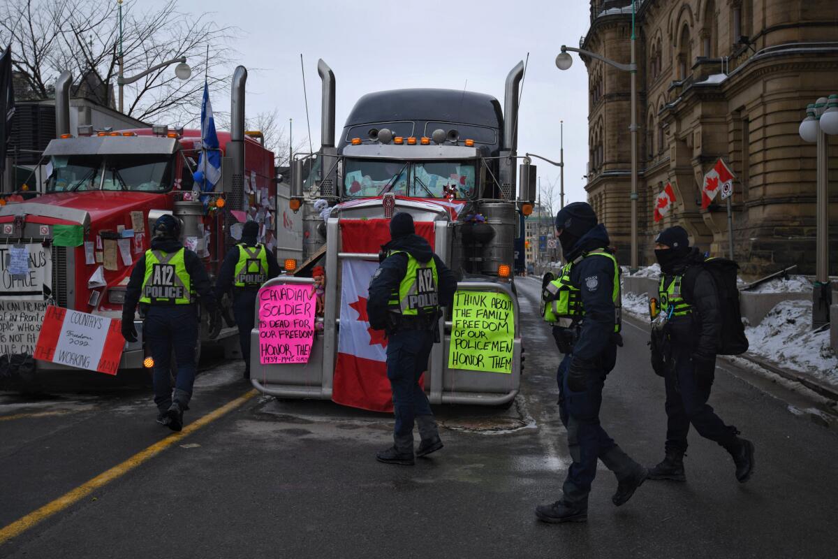 Police officers walk by big rigs covered in protest signs 