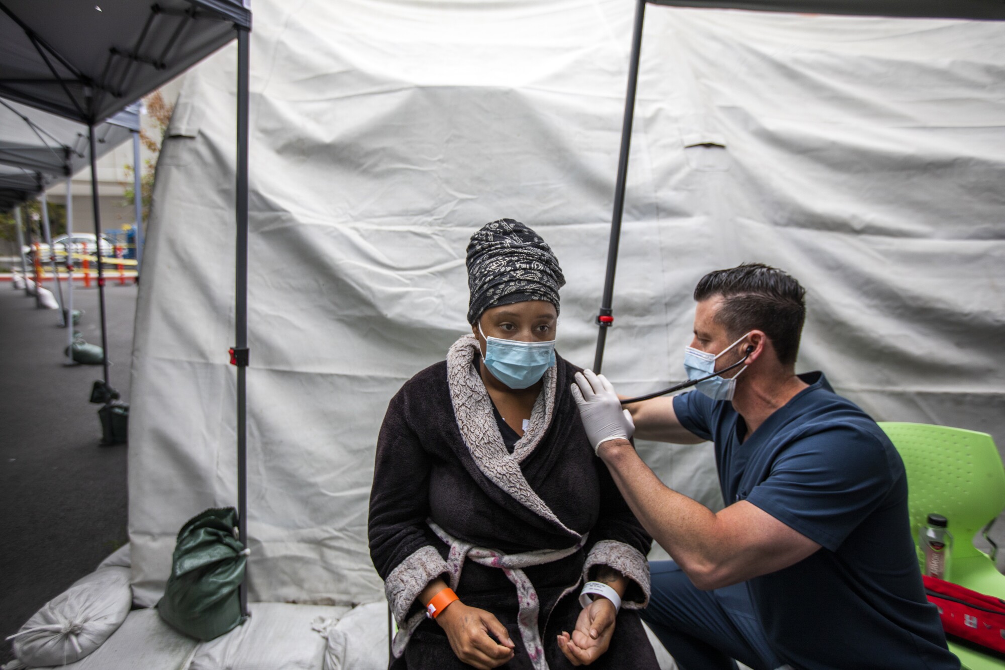 A doctor uses a stethoscope on a patient inside a tent