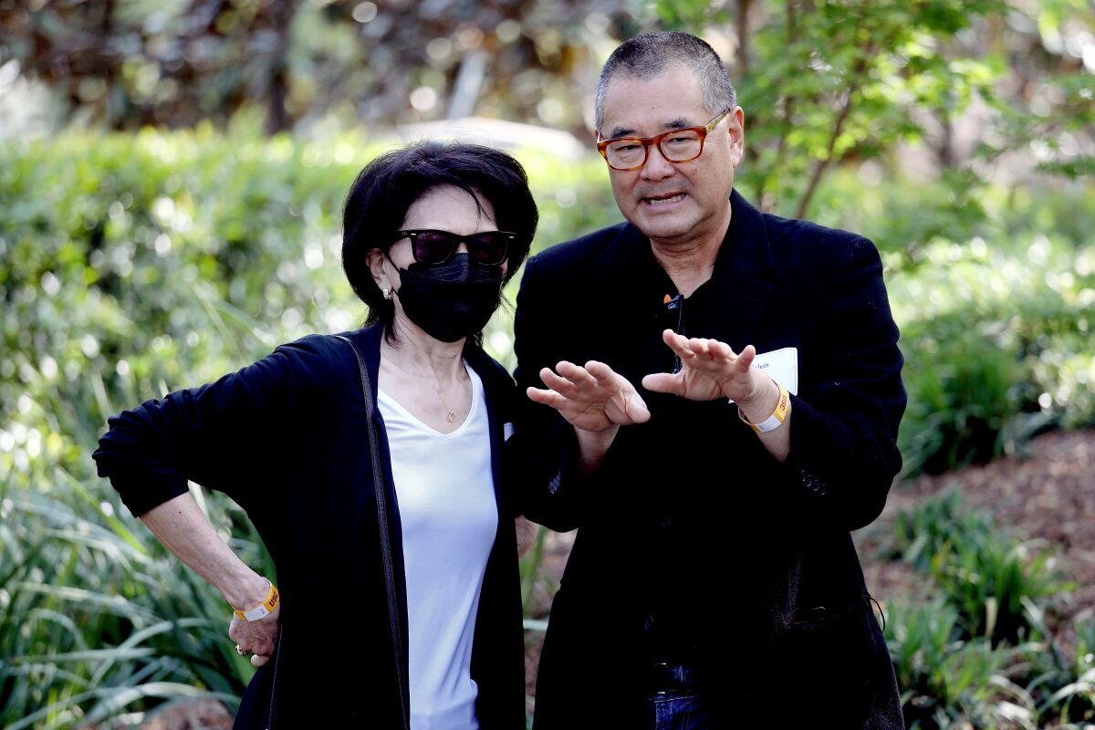 Two people speak, with plants in the background