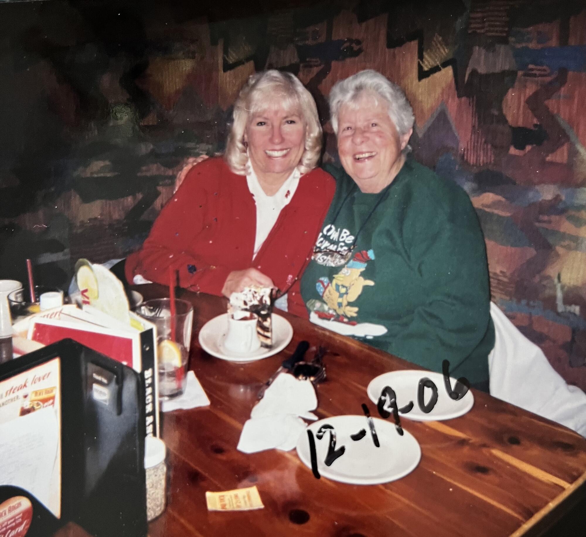 Two women smile and hug while sitting at a table.