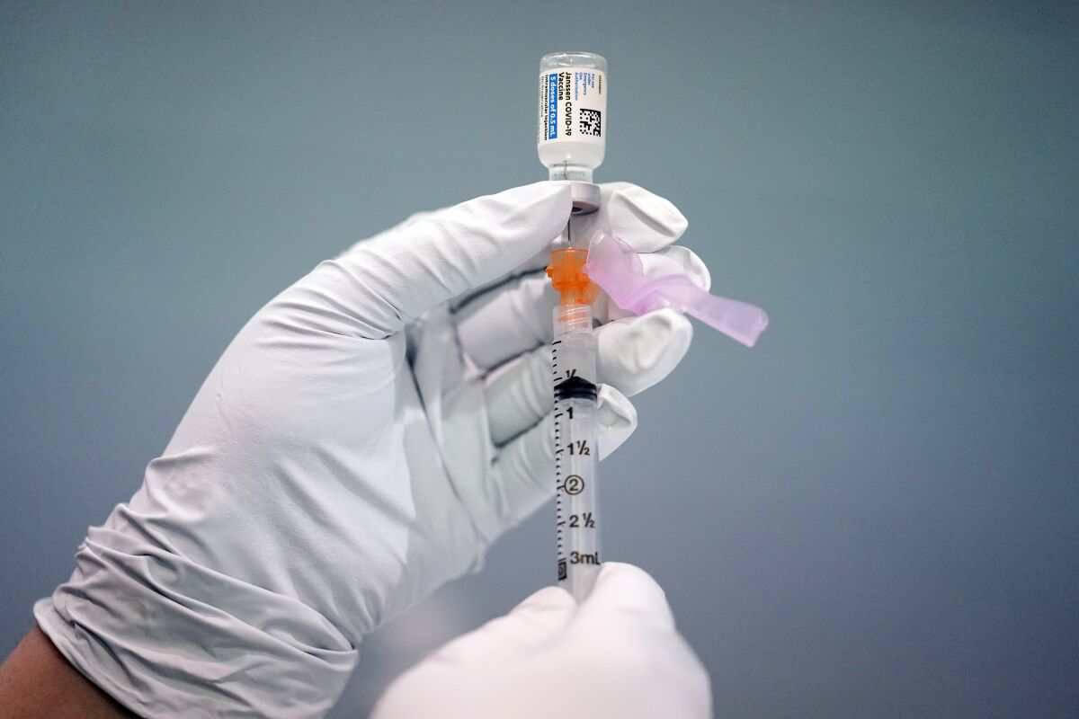 A close-up look at gloved hands loading a syringe with a dose of the Johnson & Johnson COVID-19 vaccine
