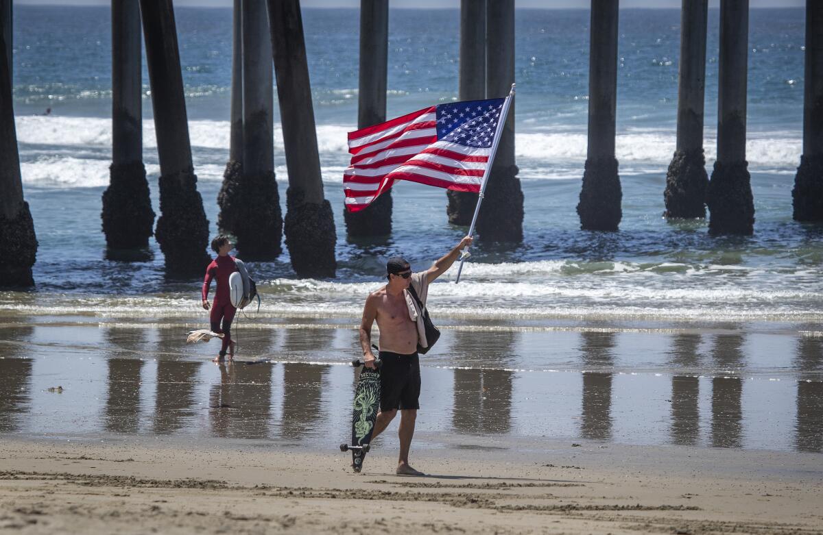 Gareth Davies, of Aliso Viejo, parades the American flag while defying during a rally to call on Gov. Newsom to relax the state's stay-at-home order on Friday in Huntington Beach.
