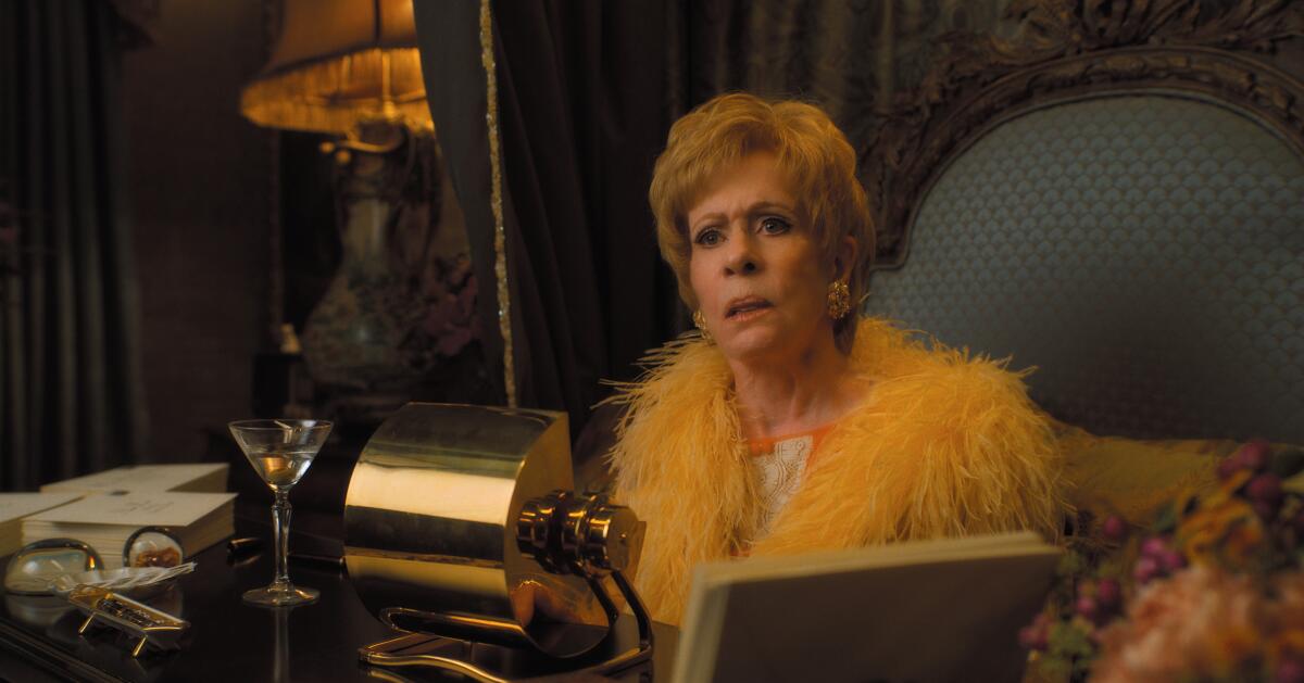 A woman in a feather robe sitting at a desk.