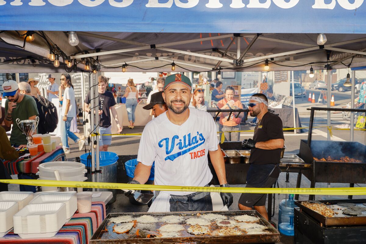 Villa's Tacos'un sahibi Victor Villa, Highland Park'ta taco standının arkasında kameraya gülümseyerek duruyor