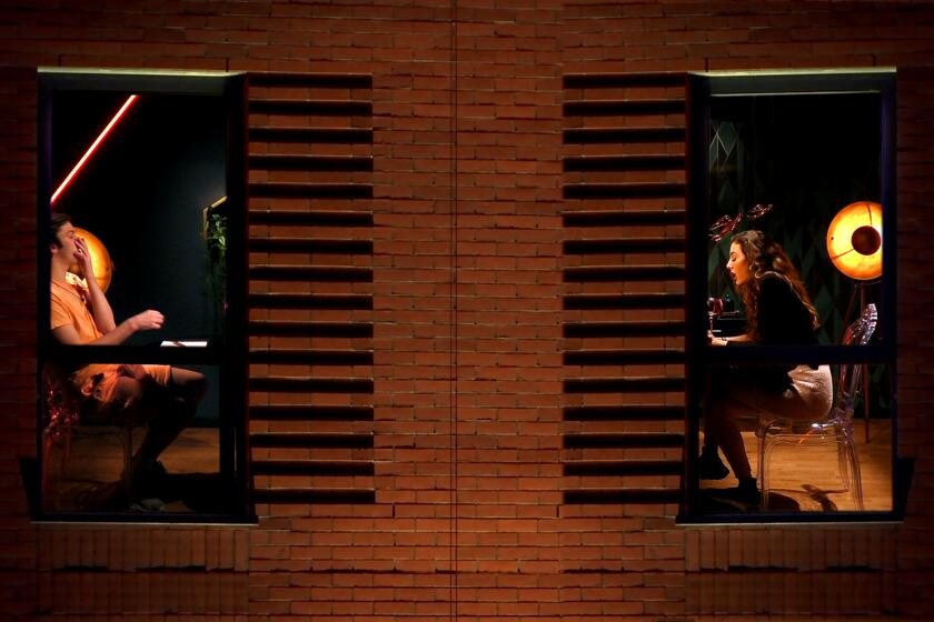 A man and a woman in separate apartments, pictured through their windows