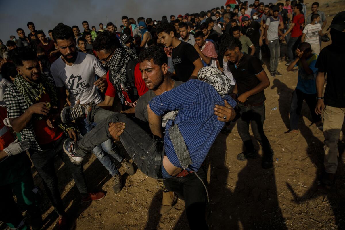 A Palestinian man carries a fellow protester after he was shot in the foot during a protest at the border fence.