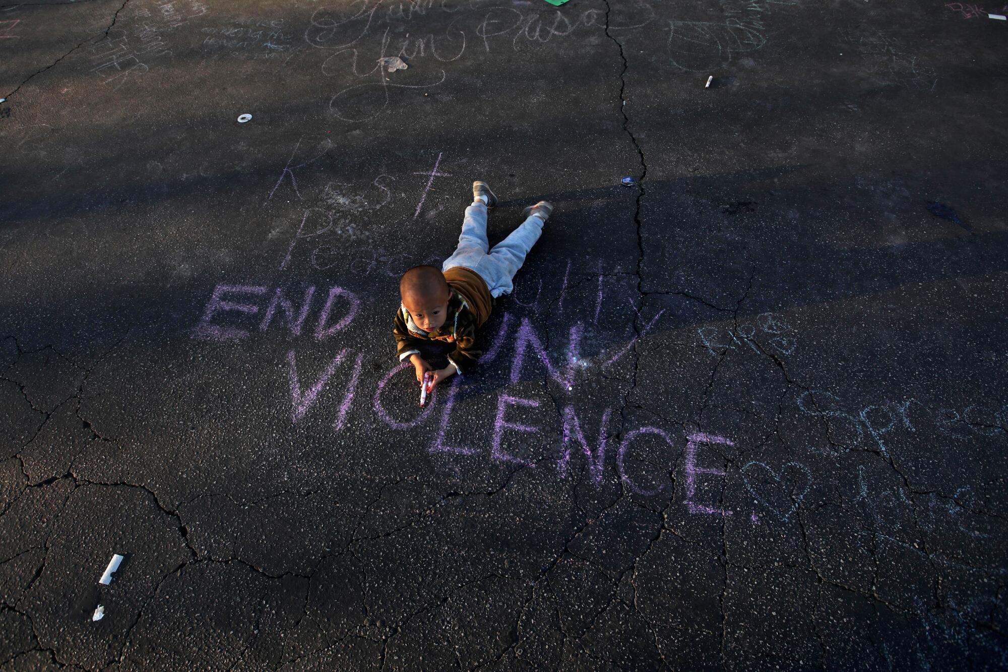 A young child lies on pavement with chalk writing that reads "End Gun Violence" 