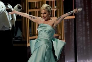 A blonde woman with a turquoise dress and tattoos performs at an awards ceremony