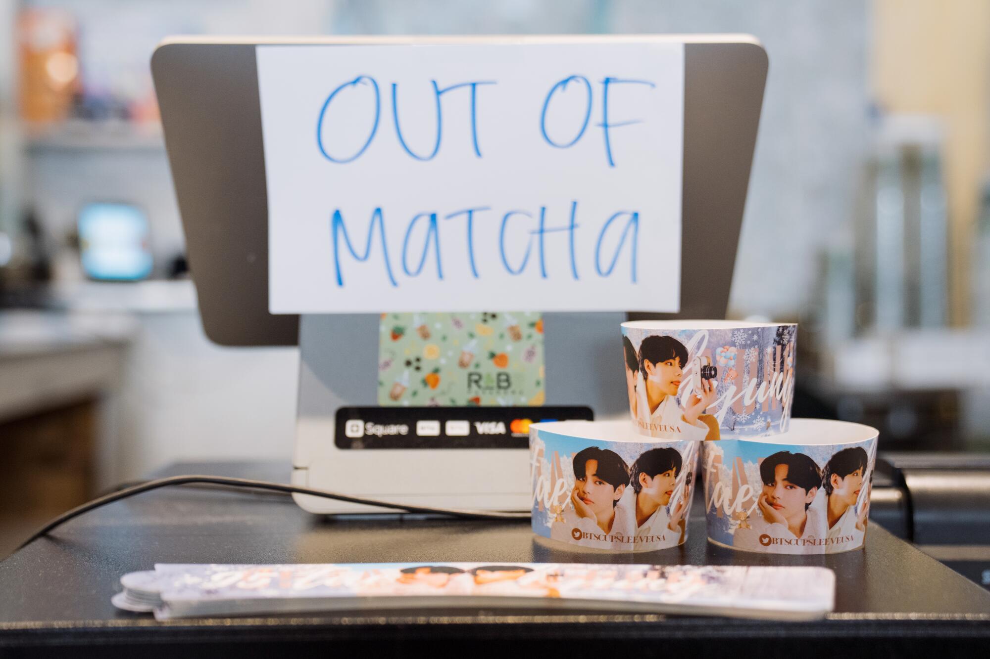 Cupsleeves with photos of Korean pop stars stacked next to a register with a sign that says Out of matcha