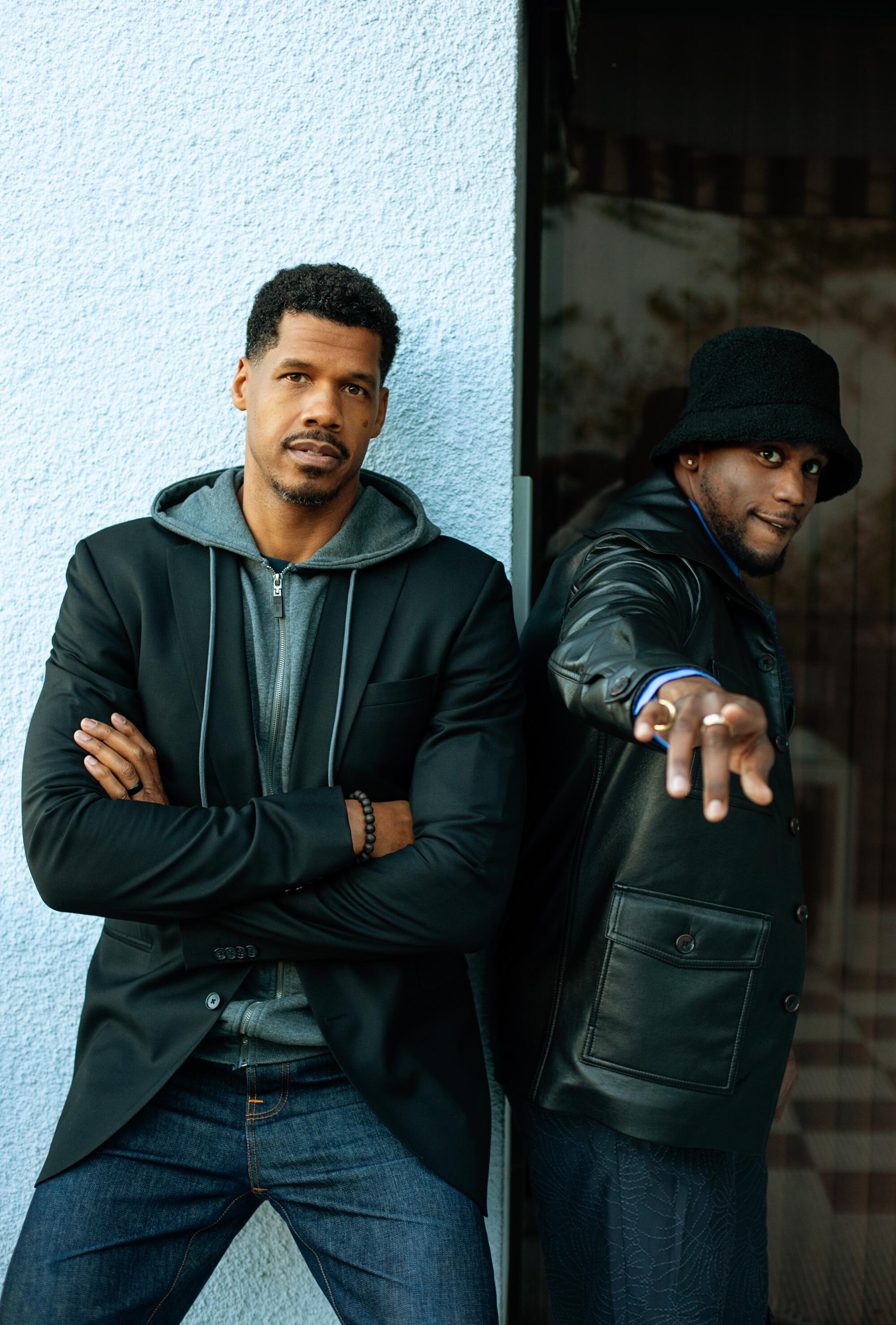 Two young men, one leaning against a wall, the other pointing at the camera.