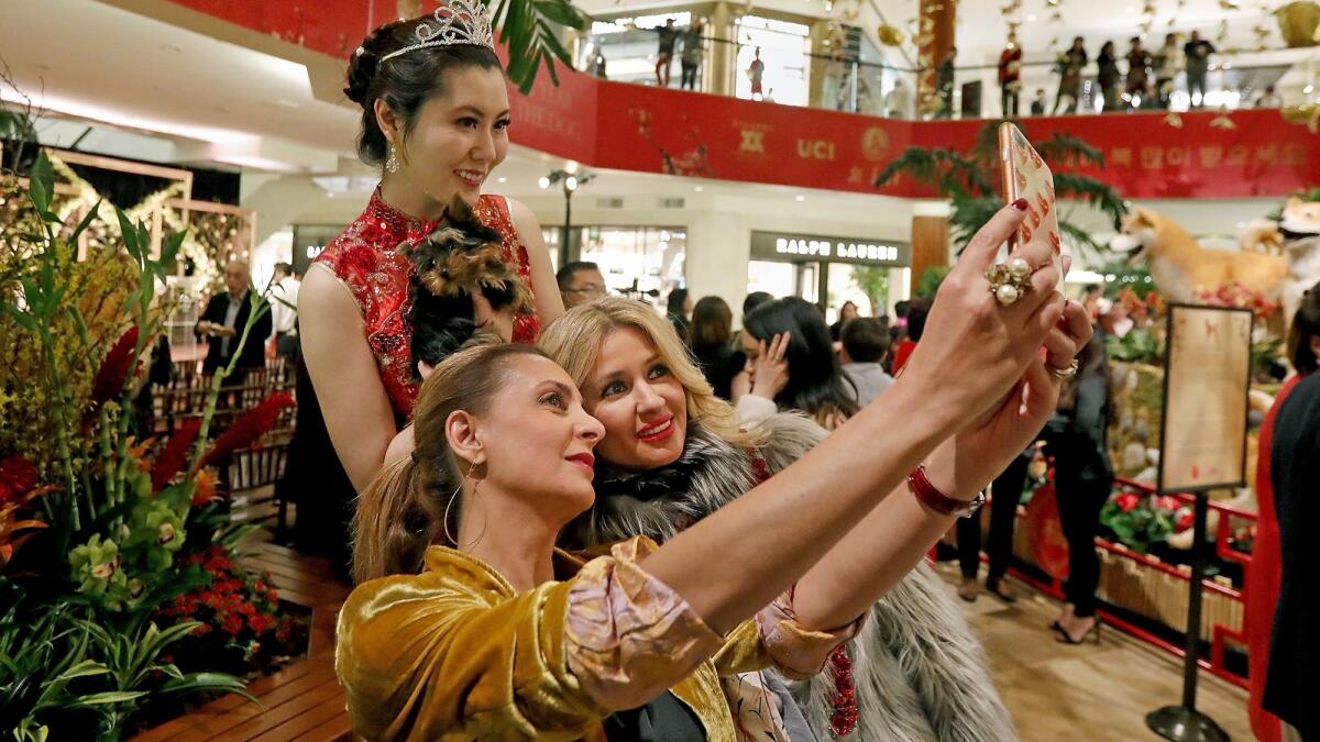 Sabrina Azadi, bottom left, and Suzan Sadeghi, bottom right, take a photo with a model holding a Yorkshire terrier during South Coast Plaza’s 2018 Lunar New Year celebration, The Year of the Dog, on Tuesday night.