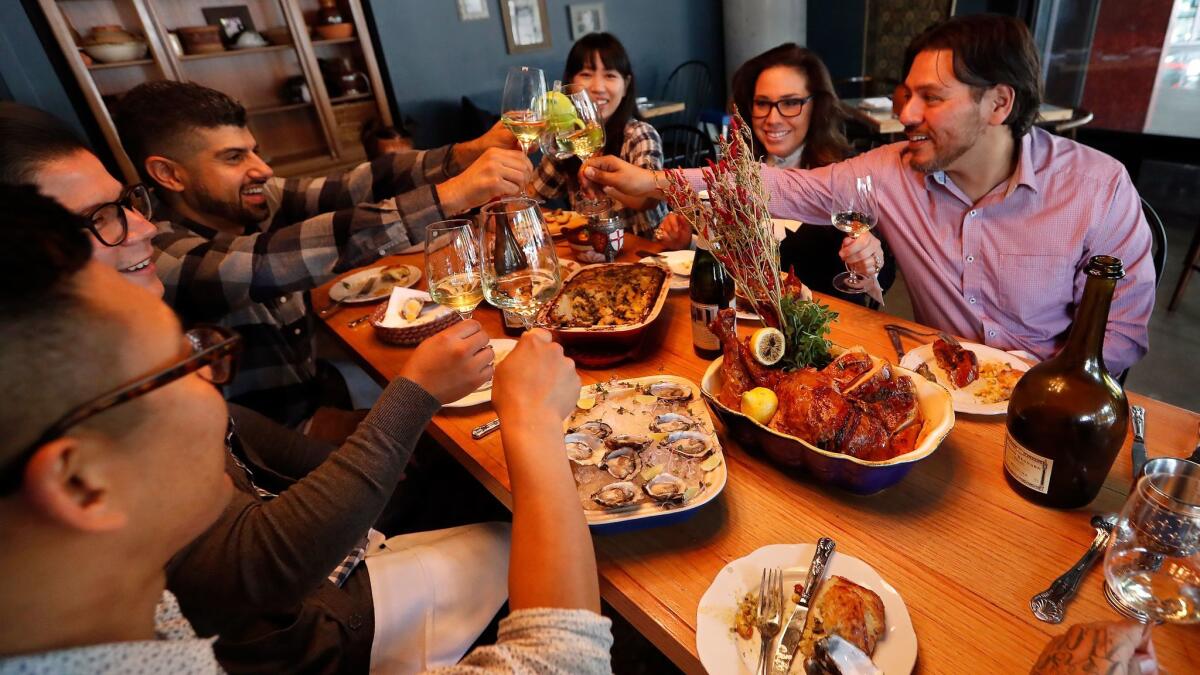 Chef Ray Garcia, right, clicks glasses with from left to right-Brian Lee, Ivan Marquez, Jason Mattick, his wife Wendy Mattik, and Ray's wife Maeria Paez, at the Thanksgiving table inside his restaurant, Broken Spanish, located in downtown Los Angeles.