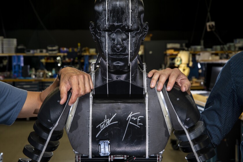 Both human hands rest on the shoulders of the signature humanoid robot.