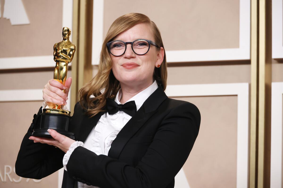 Sarah Polley wearing a tuxedo and glasses while hoisting an Oscar trophy