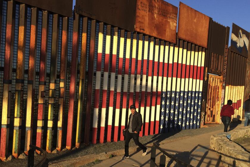 ADDS INFORMATION ABOUT THE MURAL - People walk past a mural painted on a border structure in Tijuana, Mexico, on Wednesday, Jan. 25, 2017. The mural, entitled “SOS, Deported Veterans,” was painted in 2013 by artist Amos Gregory to help raise awareness of the plight of deported veterans. President Donald Trump moved aggressively to tighten the nation's immigration controls on Wednesday, signing executive actions to jumpstart construction of his promised U.S.-Mexico border wall and cut federal grants for immigrant-protecting "sanctuary cities." (AP Photo/Julie Watson)