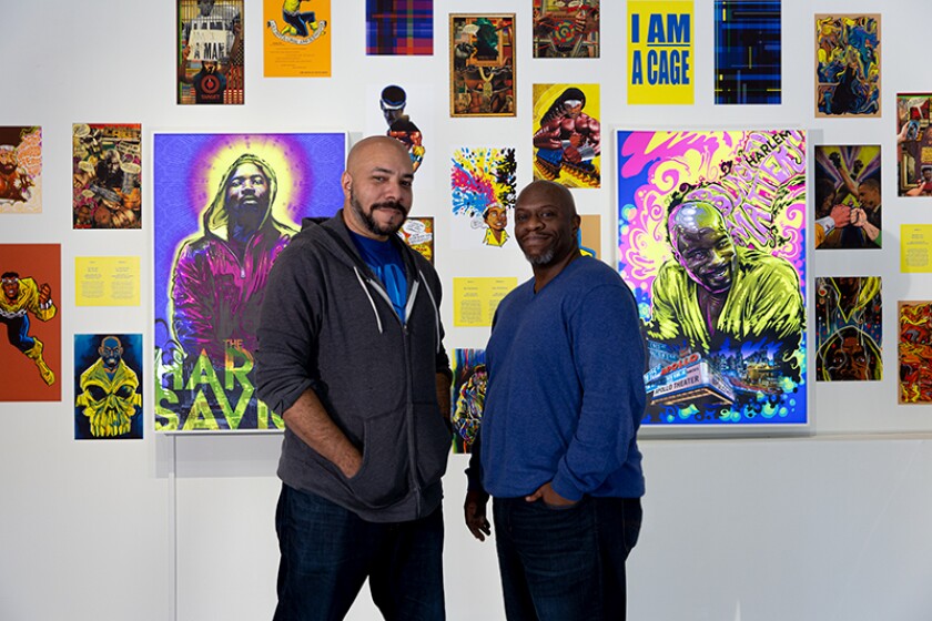 Two men stand in front of a wall of colorful illustrations 