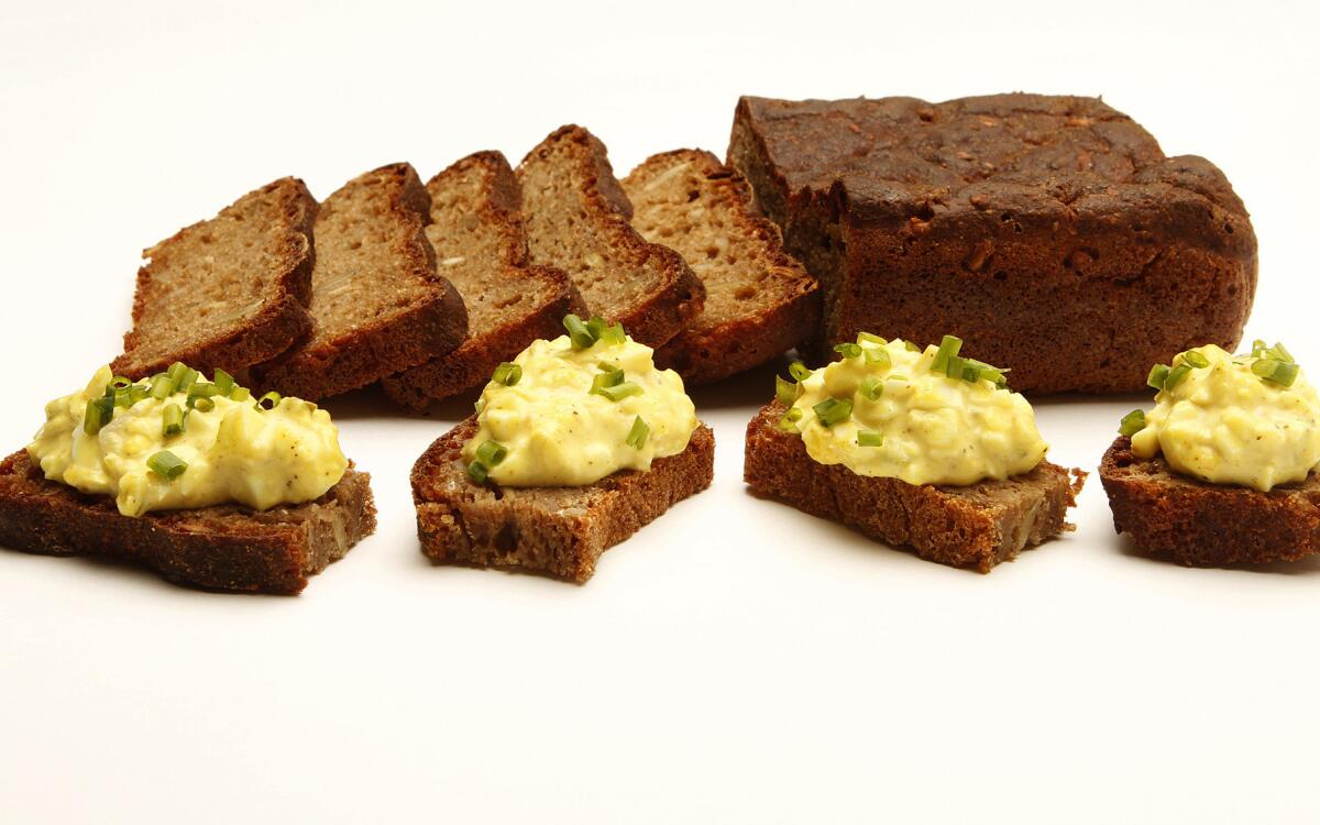 A loaf of Danish rye bread, with slices piled with egg salad and chopped chives