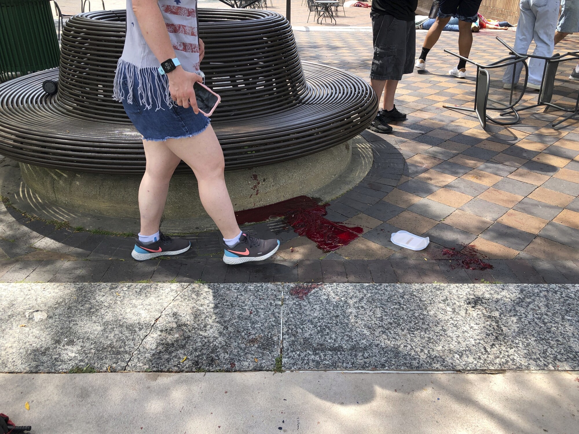 A person stands near a pool of blood on the sidewalk.
