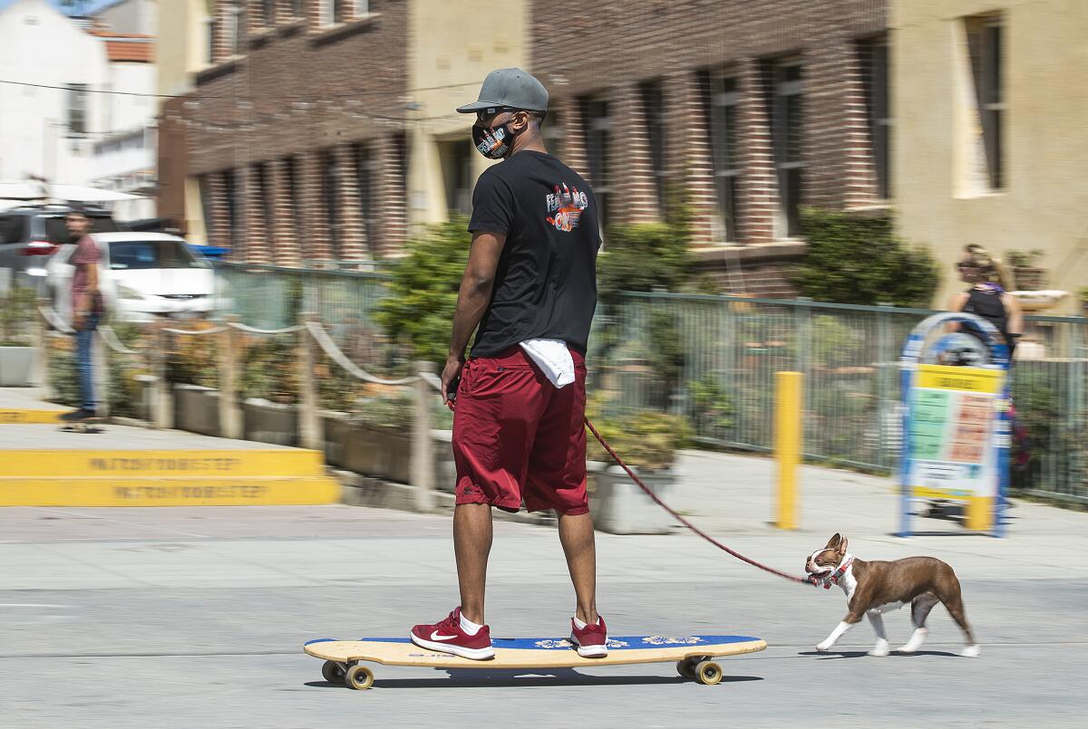 A man on a skateboard leads his leashed Boston terrier on the Venice boardwalk