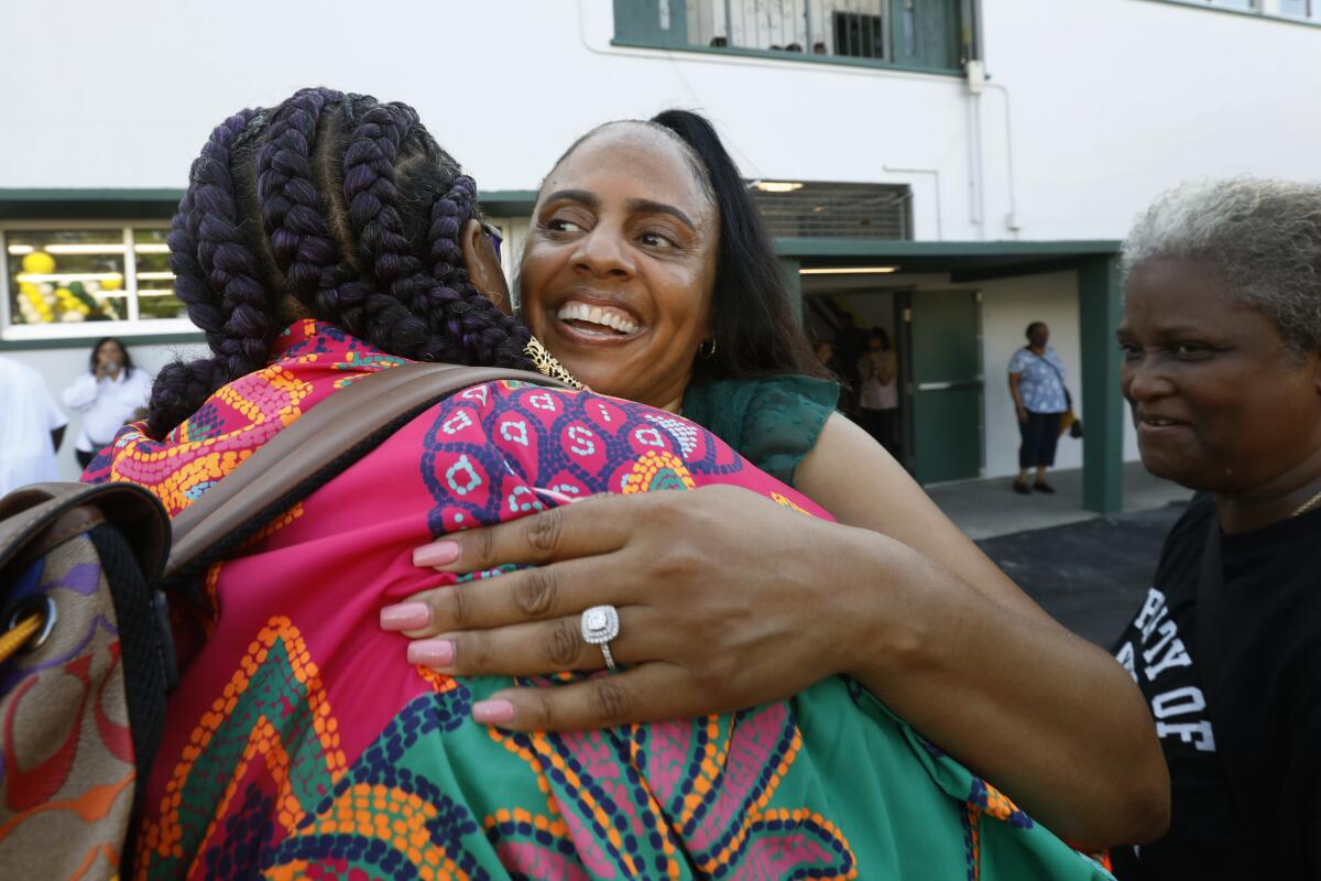 A female school principal hugs a woman in a crowd of parents, teachers, staff and students