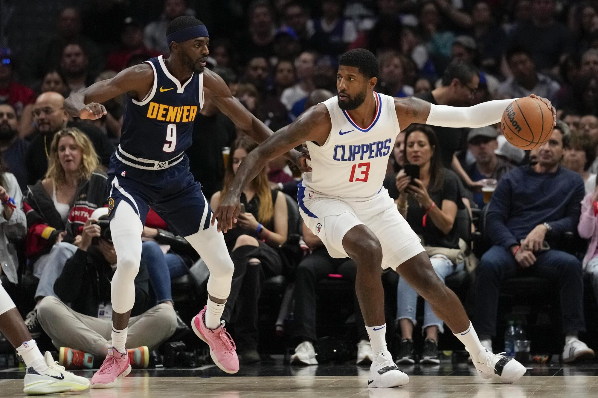 Clippers forward Paul George, right, backs down Nuggets guard Justin Holiday while dribbling with his left hand.