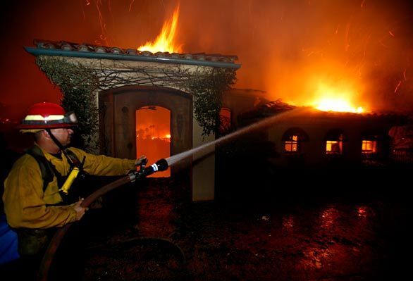 A firefighter sprays water on a burning house in Montecito where more than 100 homes burned during the fast moving Tea Fire.