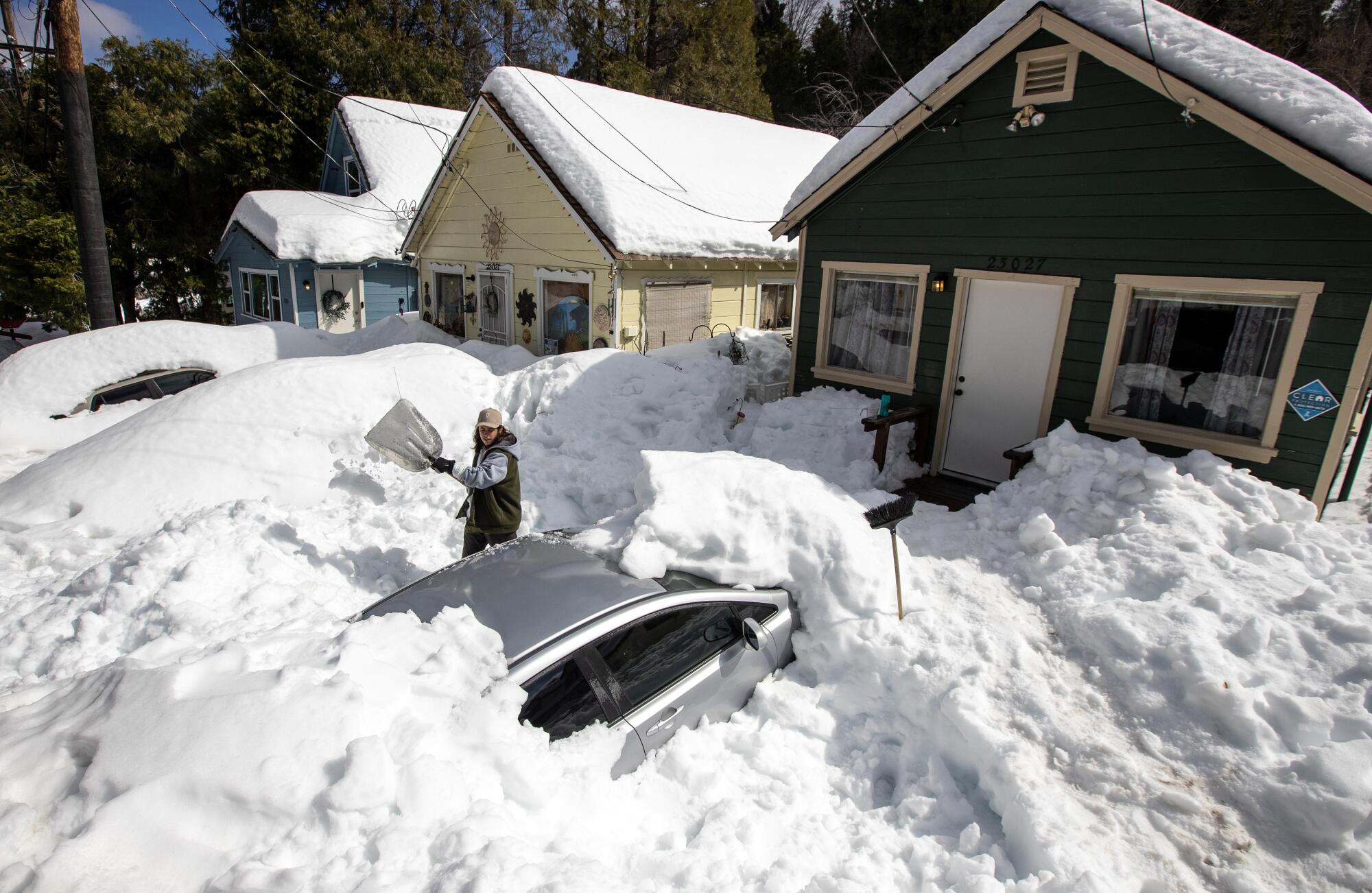 A person shovels snow that has buried a car.