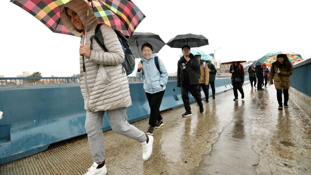 Visitors Victoria Kirilovska, left, and Zhanna Sazbassova brave the Santa Monica Pier in heavy rain Thursday. A fierce storm is expected this weekend.