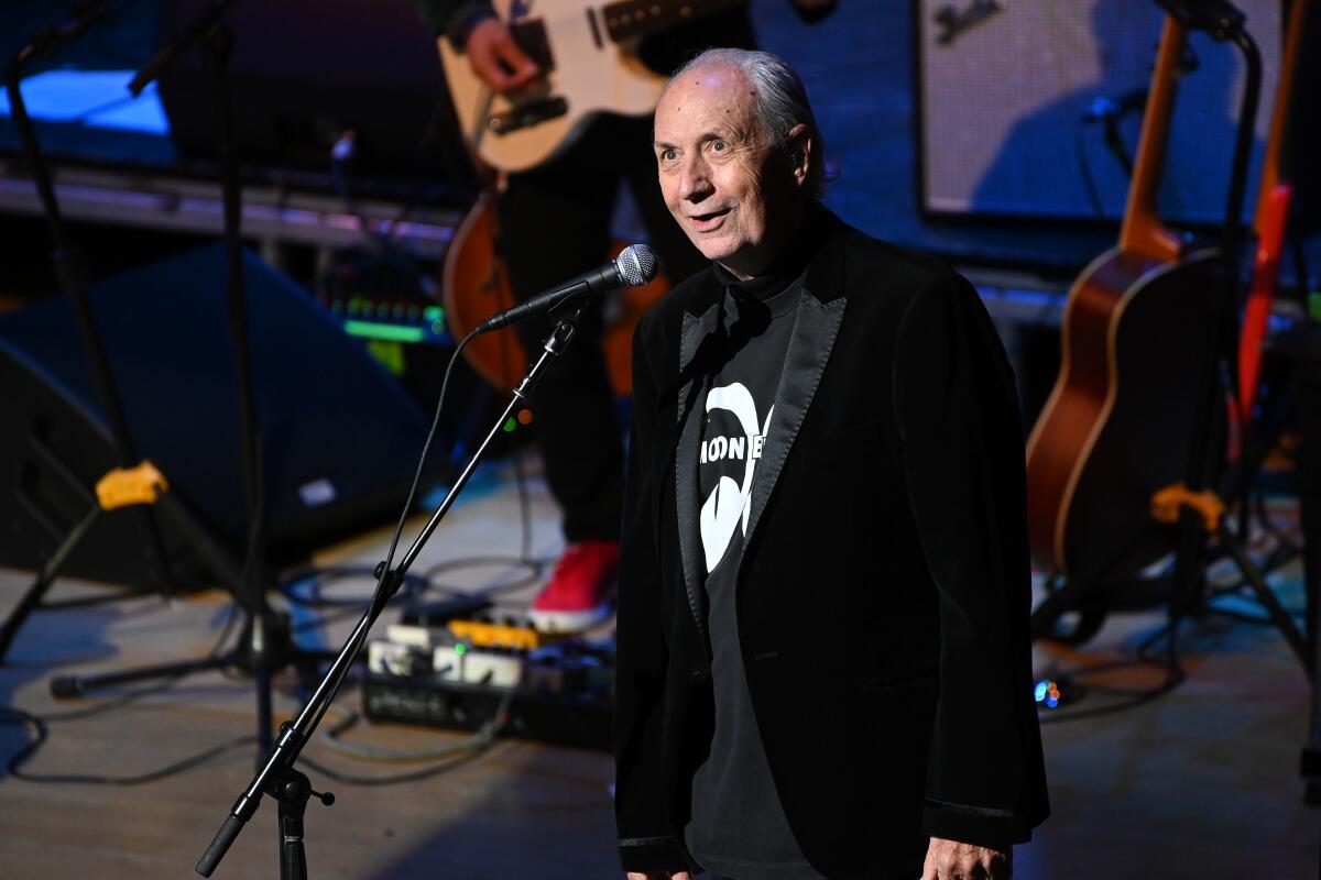 A older male singer in a black jacket stands on stage.