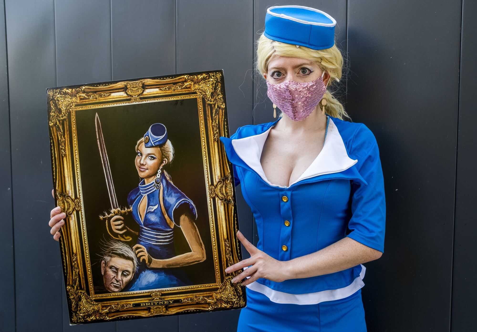 A woman in a blue flight attendant costume holds a painting of Britney Spears