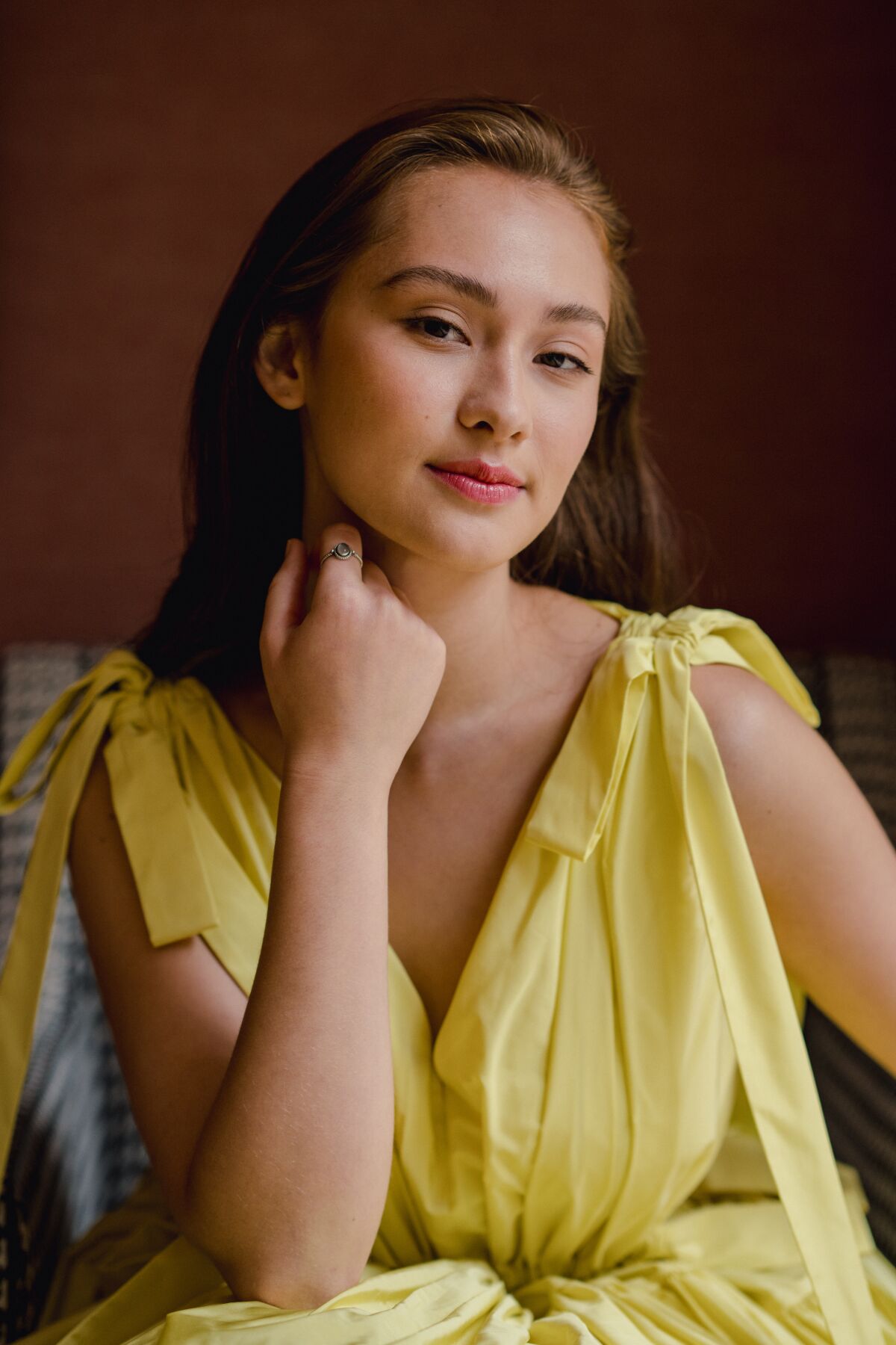  Lola Tung in a yellow dress with her hand near her neck.