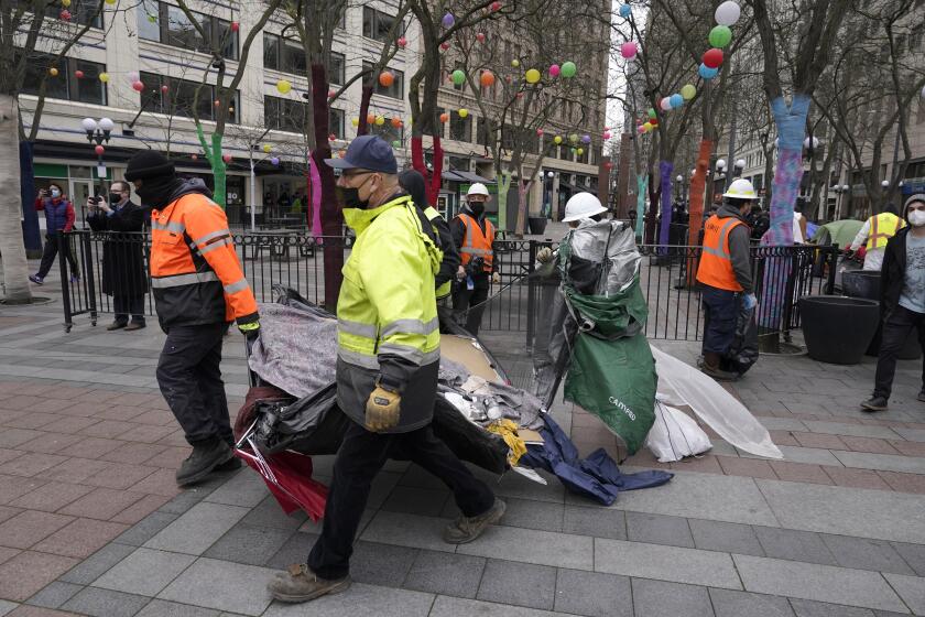 Workers carry a tent used by people experiencing homelessness to a garbage truck, Friday, March 11, 2022, during the clearing and removal of several tents at an encampment in Westlake Park in downtown Seattle. Increasingly in liberal cities across the country — where people living in tents in public spaces have long been tolerated — leaders are removing encampments and pushing other strict measures to address homelessness that would have been unheard of a few years ago. (AP Photo/Ted S. Warren)