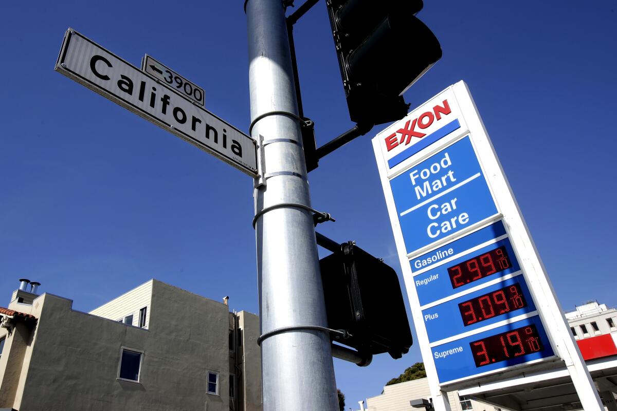A street light with a sign that says California, near an Exxon gas station sign listing prices