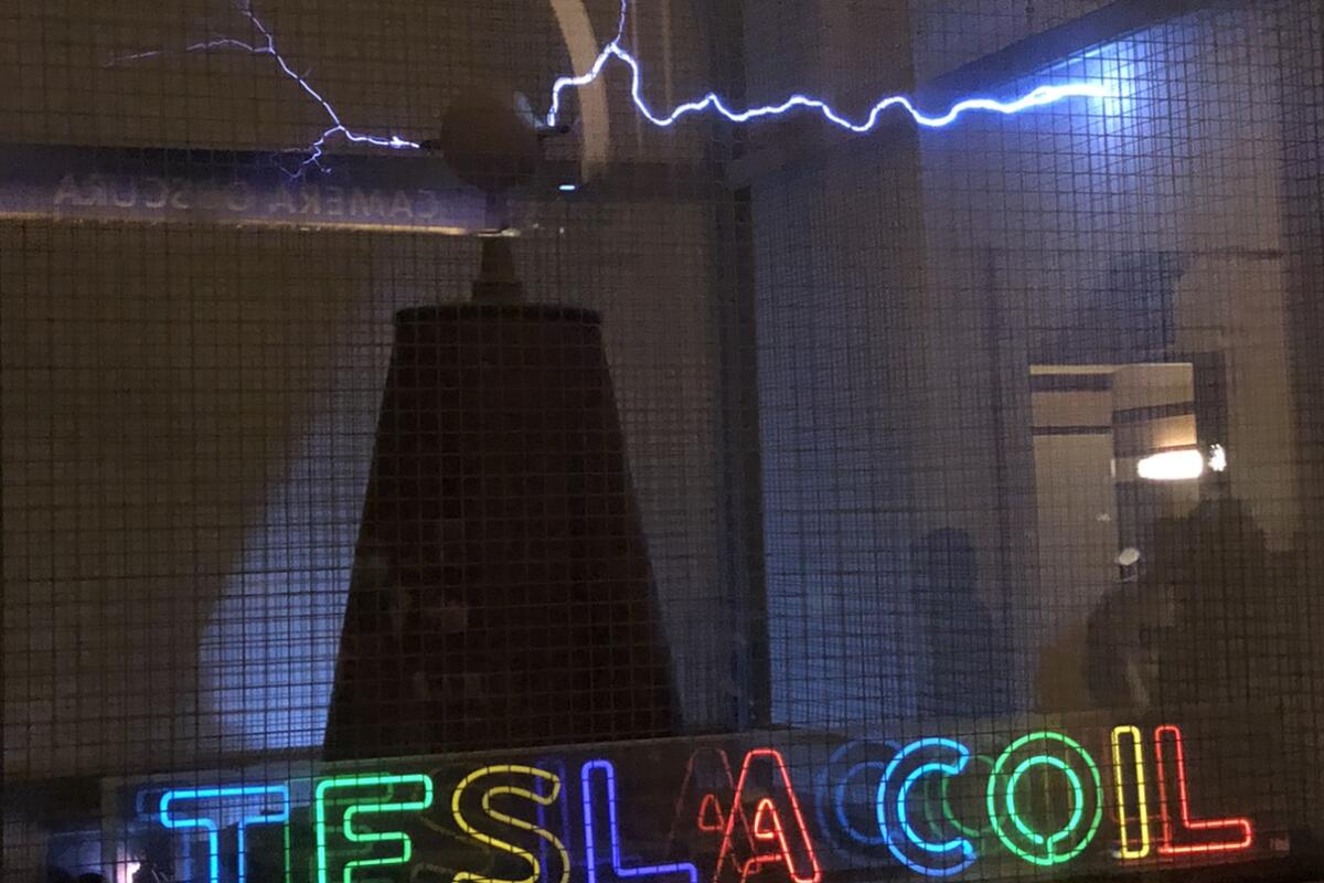 A neon sign that reads Tesla coil and sparks of electricity radiating from a cone.