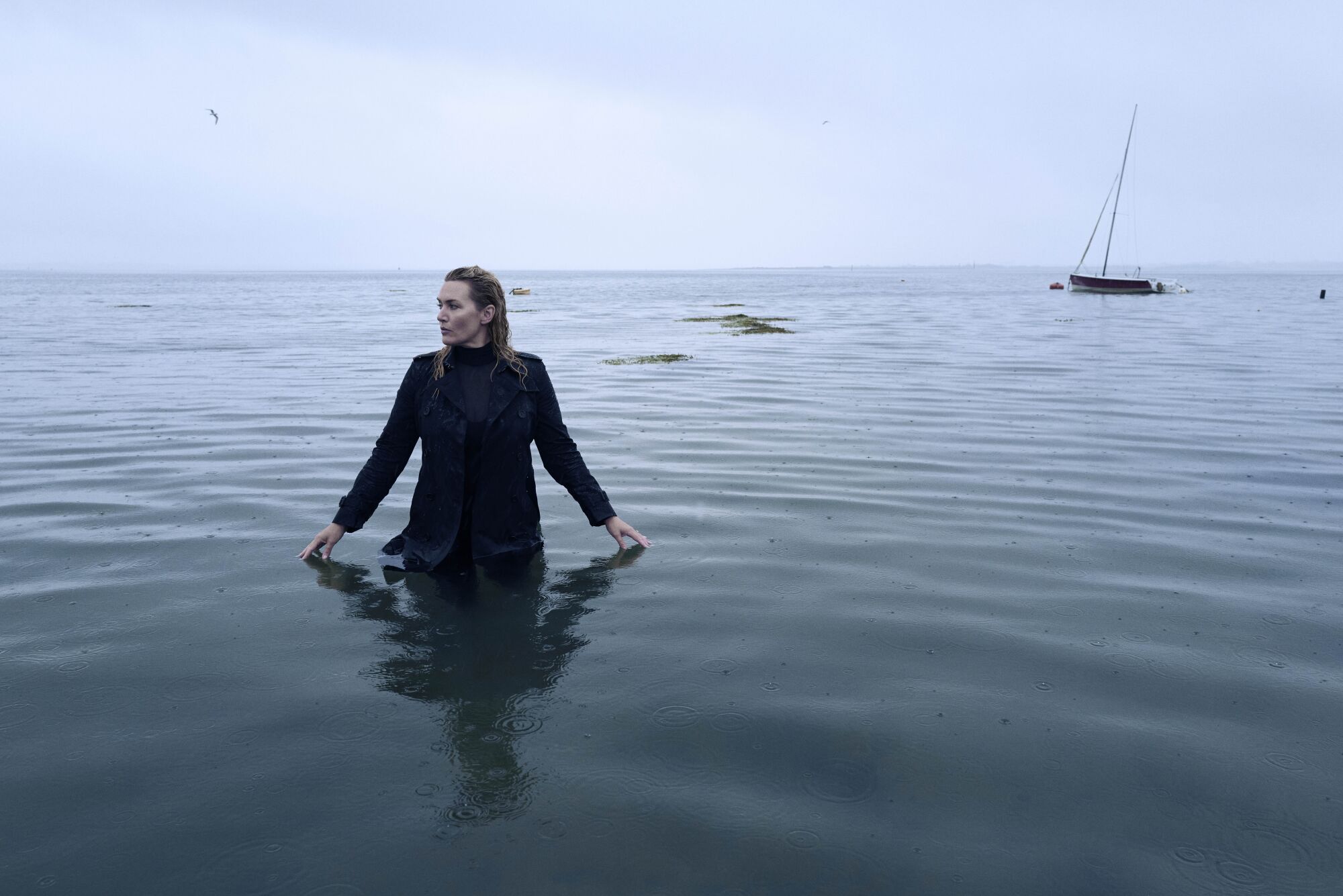 Actress Kate Winslet wading in a body of water on a gray day