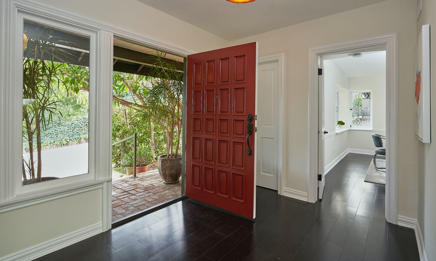 From inside, a view of the open front door, dark wood floors and adjoining light-filled room.