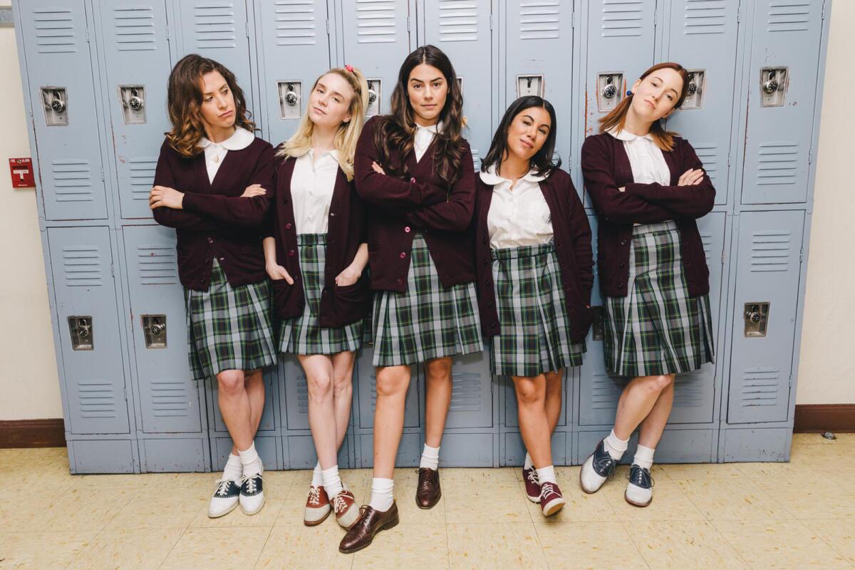 Five young women in plaid skirts, white blouses and cardigans lean against a bank of school lockers.