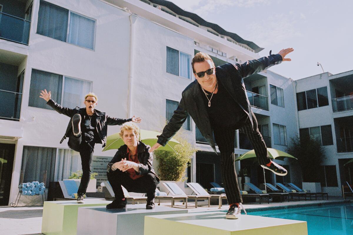 Three members of a rock band pose by a swimming pool.