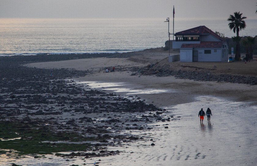 couple walk along the beach at low tide as the sun sets on Monday.