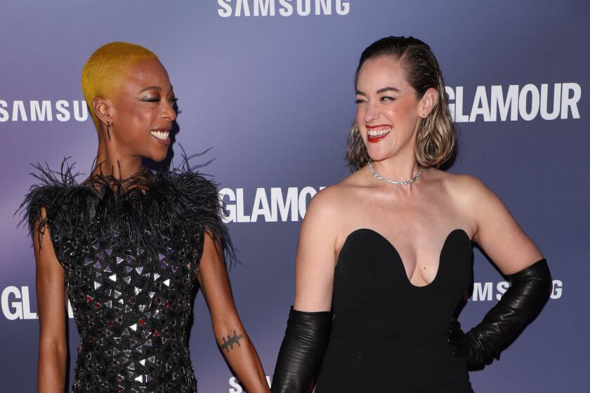 Samira Wiley smiling and holding hands with Lauren Morelli both wearing black dresses on red carpet