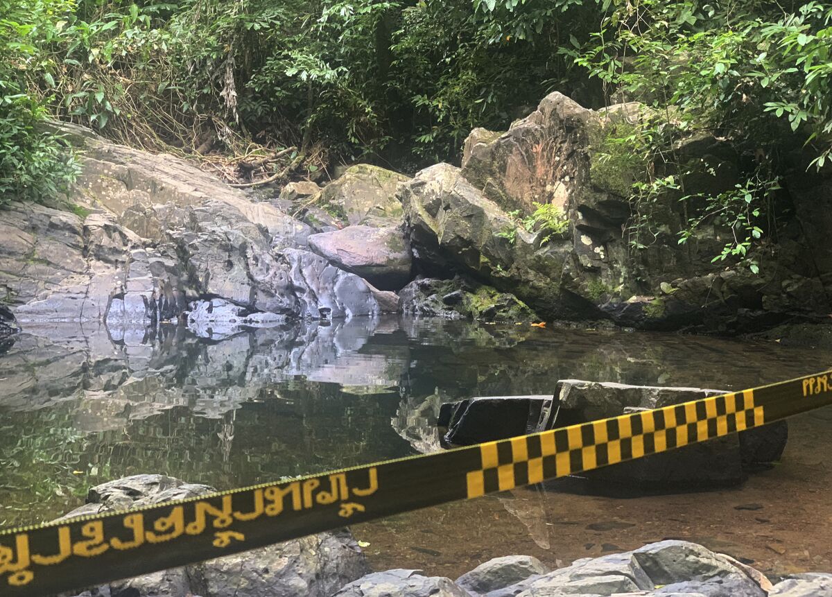 Police tape is stretched in front of a pond surrounded by rocks.
