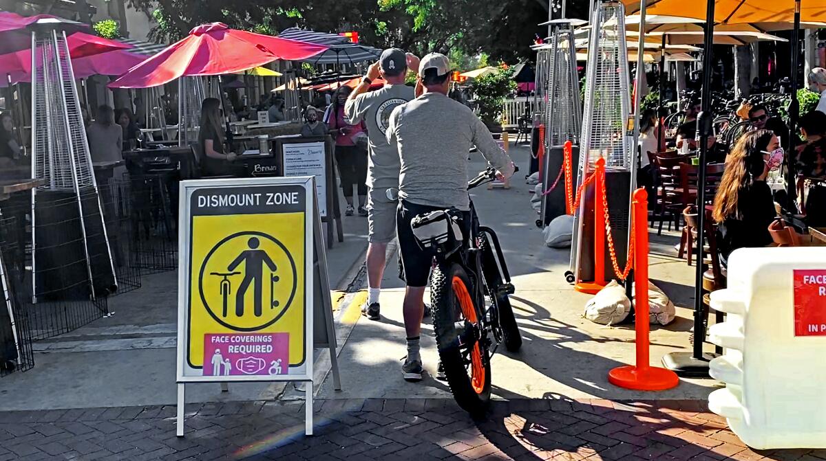 Pedestrians and cyclists share a pathway between outdoor dining areas in Santa Barbara