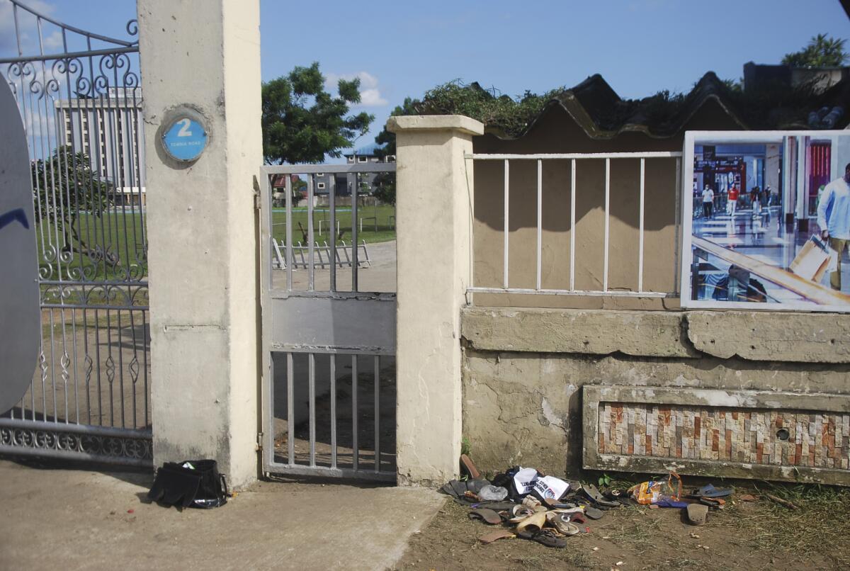 Sandals are piled outside a gate in an outdoor area. 