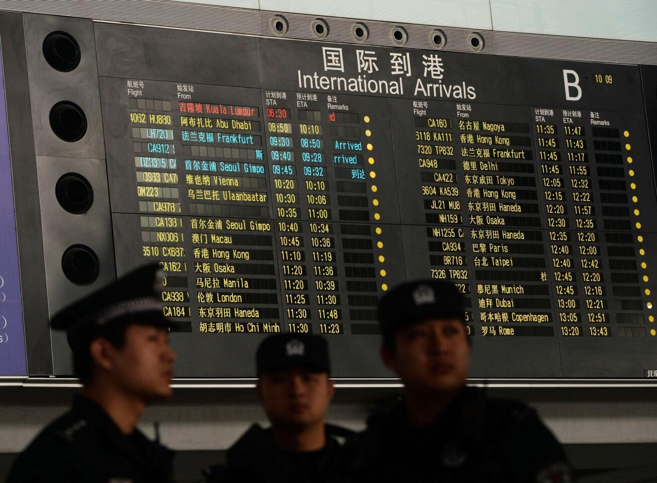 Chinese police stand beside the arrival board showing the flight MH370 (top-red) at the Beijing Airport after news of the Malaysia Airlines Boeing 777-200 plane disappeared.